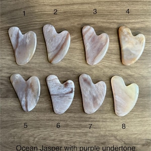 May include: Eight heart-shaped ocean jasper gua sha tools with purple undertones. The tools are arranged in two rows of four, numbered 1 through 8.
