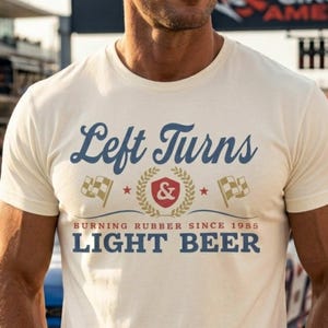 May include: Cream-colored t-shirt with the text "Left Turns & Burning Rubber Since 1985 LIGHT BEER" in navy blue and red. The design includes checkered flags and a laurel wreath. The shirt is a casual wear item.