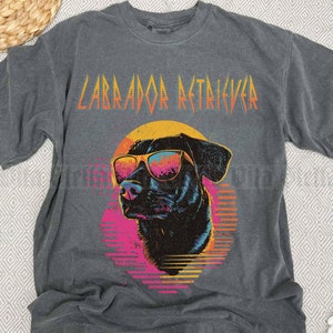 Puede incluir: Una camiseta gris oscuro con un gr&aacute;fico retro de un Labrador Retriever con gafas de sol. El texto "Labrador Retriever" est&aacute; impreso en negrita, en negro, sobre el perro.