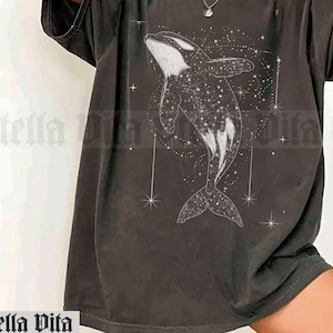 May include: An oversized t-shirt in a dark grey colour with a white graphic of an orca whale swimming through a field of stars.