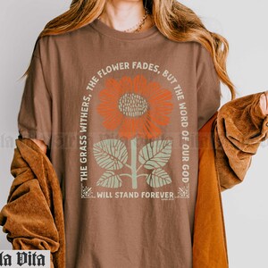 May include: A brown t-shirt with a graphic of a sunflower and the text "The grass withers, the flower fades, but the word of our God will stand forever."