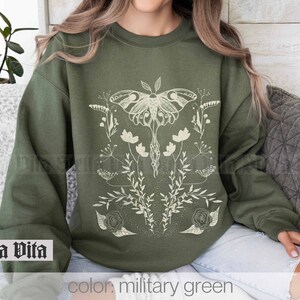 May include: A green sweatshirt with a white graphic of a moth and flowers. The text "Stella Vita" is printed on the bottom left corner of the sweatshirt. The text "color: military green" is printed on the bottom right corner of the sweatshirt.