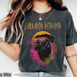 Puede incluir: Una camiseta negra con un gr&aacute;fico de estilo vintage de un Labrador Retriever con gafas de sol. El texto "Labrador Retriever" est&aacute; impreso en una fuente en negrita y met&aacute;lica sobre el perro.