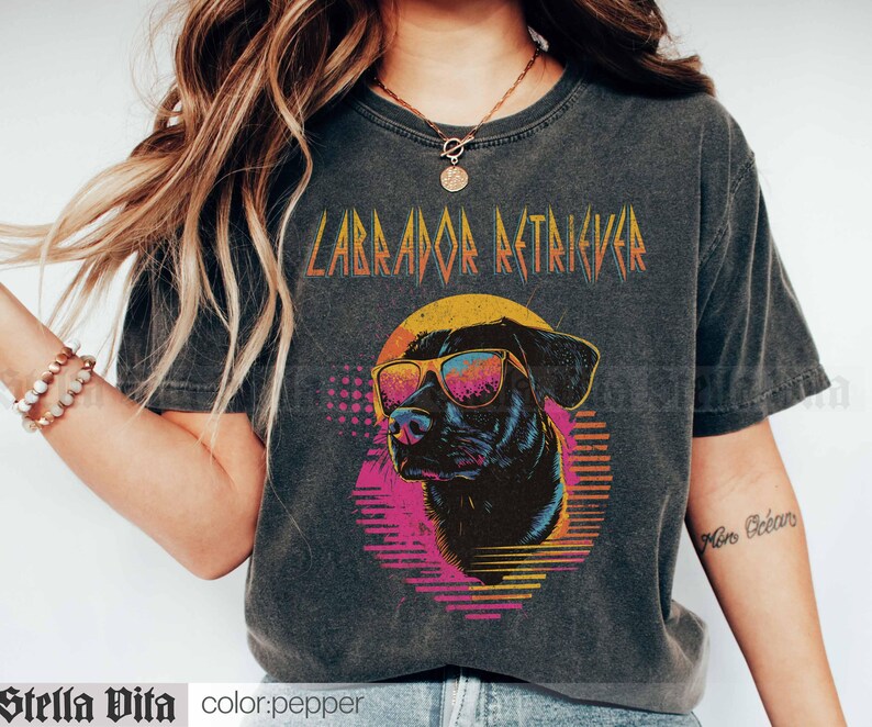 Puede incluir: Una camiseta negra con un gr&aacute;fico de estilo vintage de un Labrador Retriever con gafas de sol. El texto "Labrador Retriever" est&aacute; impreso en una fuente en negrita y met&aacute;lica sobre el perro.