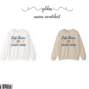 May include: Two unisex sweatshirts, one white and one tan, each displaying the text "Left Turns & Light Beer" in blue and gold. The sweatshirts are made of a soft material and are perfect for casual wear.