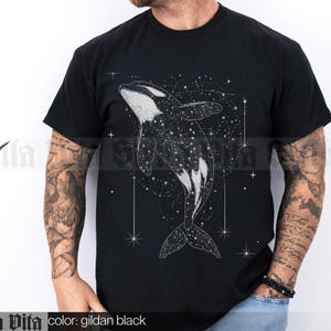 May include: Black t-shirt featuring a white graphic of an orca whale swimming in a field of stars. The text "Stella Vita" is printed on the bottom of the shirt.