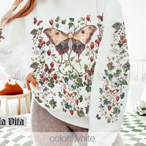 May include: White sweatshirt with a large butterfly and floral print. The butterfly is brown, green, and purple with red and white strawberries throughout the design.