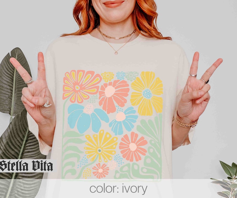 Peut inclure: Un t-shirt cr&egrave;me avec un imprim&eacute; floral color&eacute;. L'imprim&eacute; pr&eacute;sente une vari&eacute;t&eacute; de fleurs dans des tons de rose, jaune, bleu et vert. Le texte "Stella Vita" est imprim&eacute; en noir dans le coin inf&eacute;rieur gauche du t-shirt. Le texte "color: ivory" est imprim&eacute; dans le coin inf&eacute;rieur droit du t-shirt.