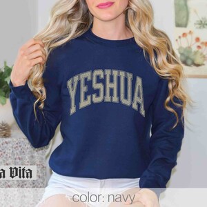 May include: Navy blue sweatshirt with the word "YESHUA" in a vintage-style white font.