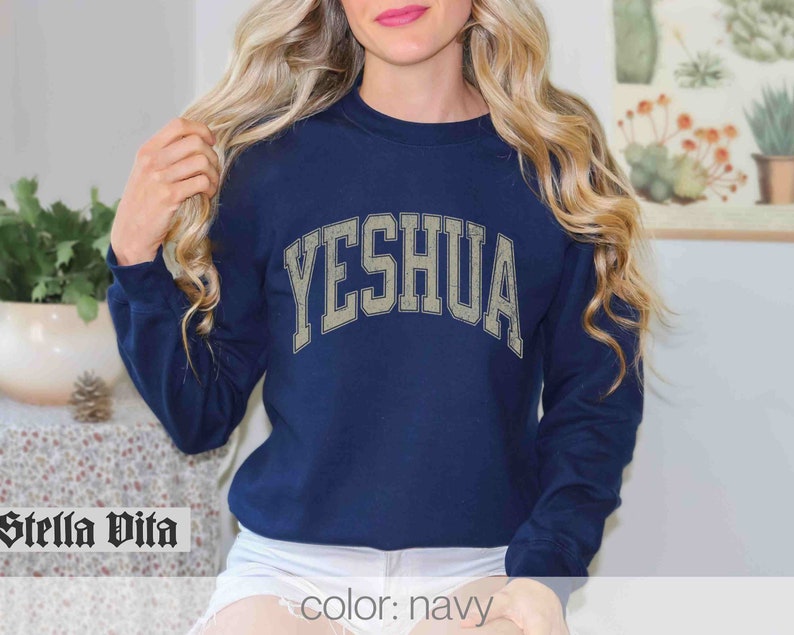 May include: Navy blue sweatshirt with the word "YESHUA" in a vintage-style white font.
