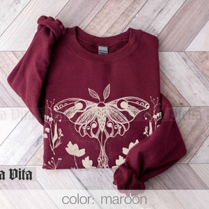 May include: Maroon sweatshirt with a white graphic of a moth and flowers. The text "Stella Vita" is visible in the bottom left corner of the image.