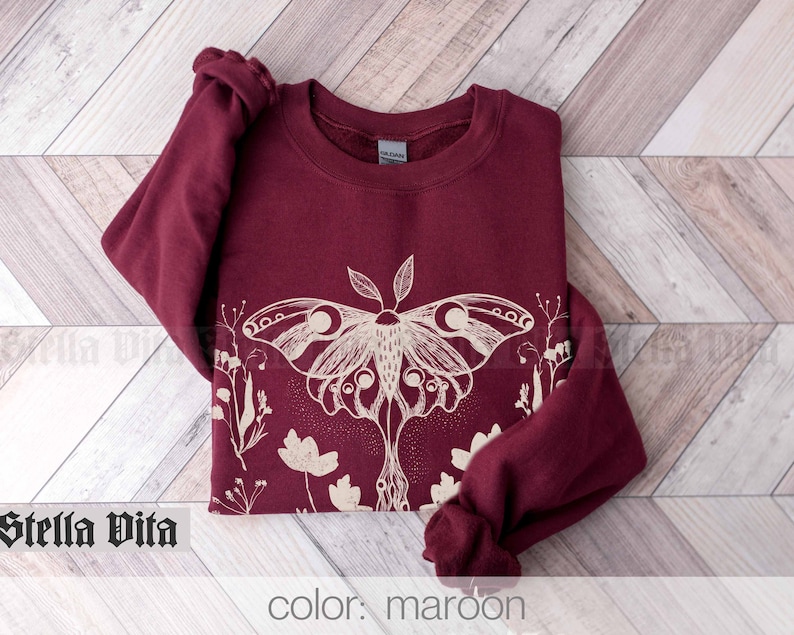 May include: Maroon sweatshirt with a white graphic of a moth and flowers. The text "Stella Vita" is visible in the bottom left corner of the image.
