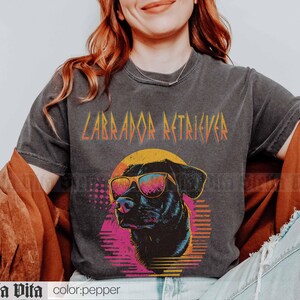 Puede incluir: Una camiseta negra con un gr&aacute;fico de un Labrador Retriever con gafas de sol y el texto "Labrador Retriever" en una fuente de metal.