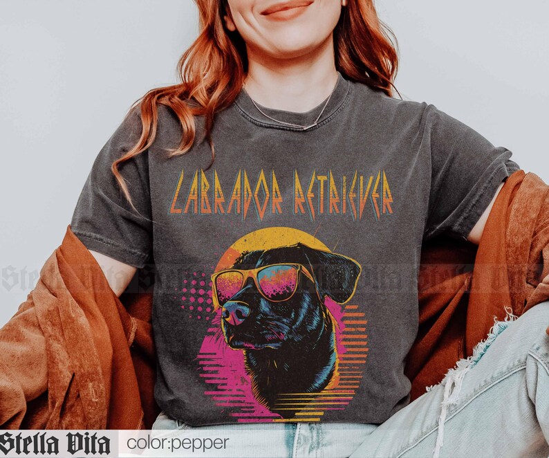 Puede incluir: Una camiseta negra con un gr&aacute;fico de un Labrador Retriever con gafas de sol y el texto "Labrador Retriever" en una fuente de metal.
