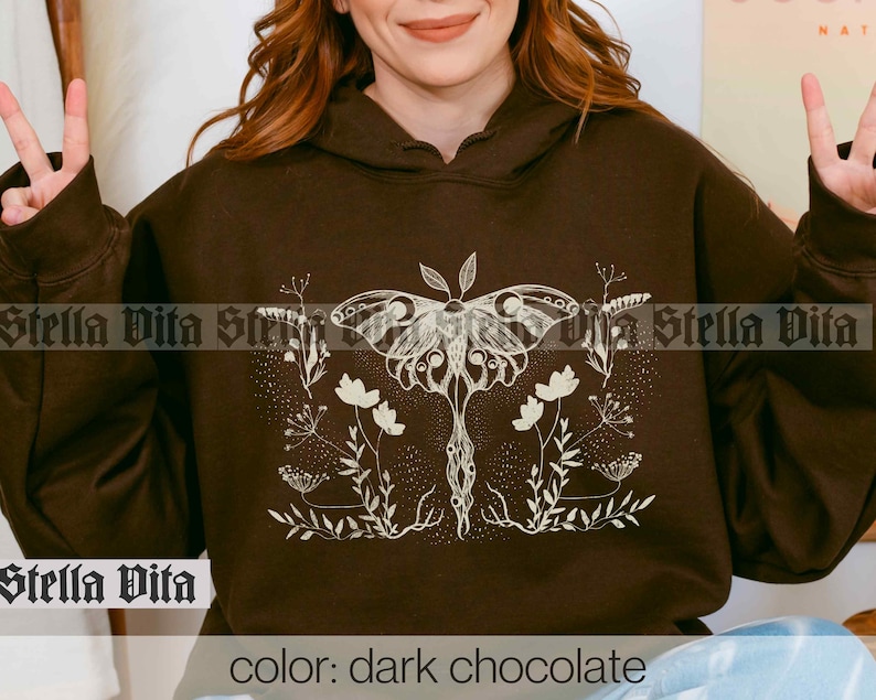 May include: A dark chocolate brown hoodie with a white graphic of a moth and floral design. The text "Stella Vita" is printed on the front of the hoodie.