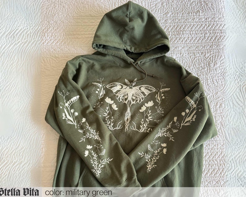 May include: A green hooded sweatshirt with a white print of a moth and flowers. The text "Stella Vita" and "color: military green" is printed on the bottom of the image.