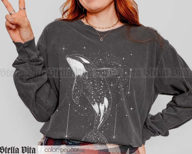 May include: A dark gray long-sleeved shirt with a white graphic of an orca whale swimming in a field of stars. The text "color: pepper" is visible at the bottom of the image.