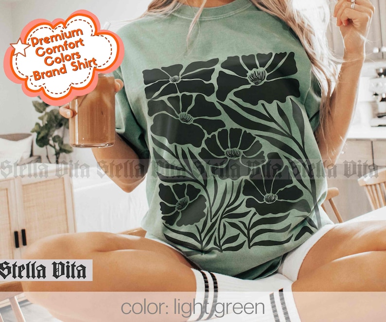 Puede incluir: Una camiseta verde claro con un dise&ntilde;o floral negro. La camiseta tiene el texto "Premium Comfort Colors Brand Shirt" en la esquina superior izquierda. El texto "color: light green" est&aacute; en la parte inferior de la imagen.