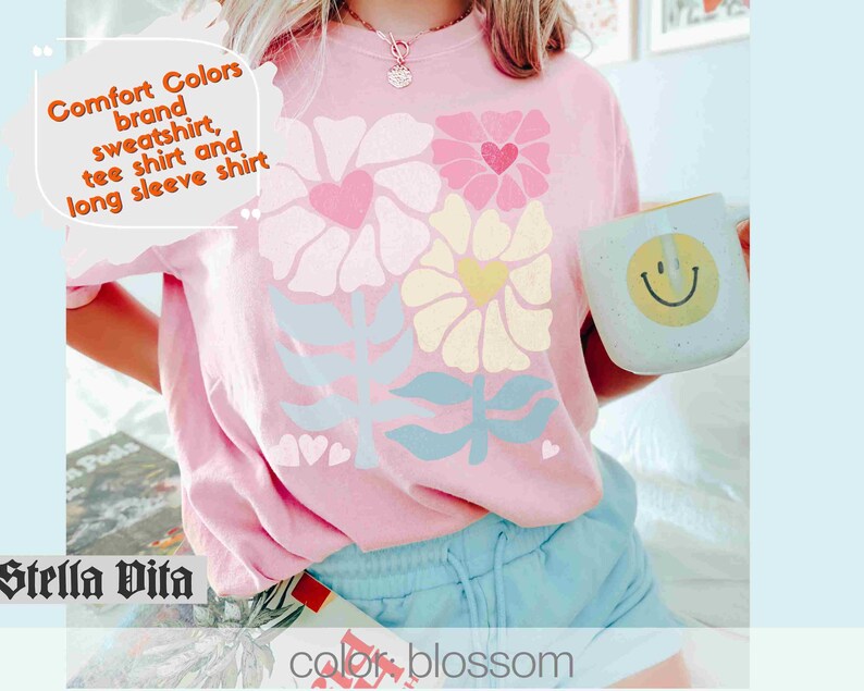 May include: A pink t-shirt with a floral design and the text "Comfort Colors brand sweatshirt, tee shirt and long sleeve shirt". The shirt is being worn by a person and has a blue and white floral design.