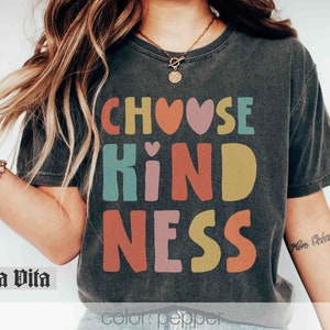 K&ouml;nnte beinhalten: Ein schwarzes T-Shirt mit dem Text "Choose Kindness" in bunten Buchstaben mit Herzen. Die Buchstaben sind in einer Schriftart im Retro-Stil.
