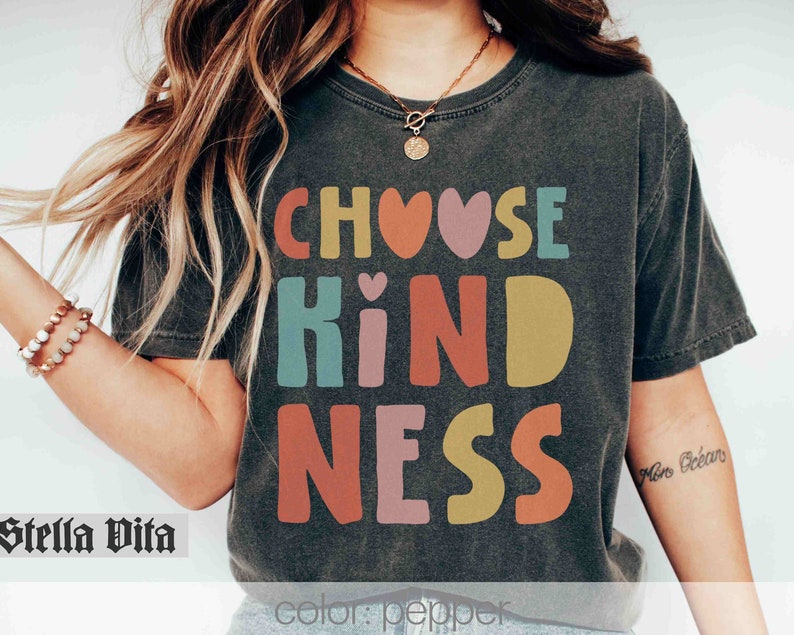 K&ouml;nnte beinhalten: Ein schwarzes T-Shirt mit dem Text "Choose Kindness" in bunten Buchstaben mit Herzen. Die Buchstaben sind in einer Schriftart im Retro-Stil.