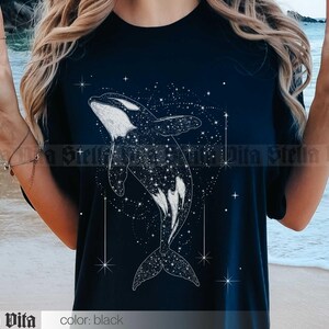 May include: A black t-shirt with a white graphic of an orca whale swimming through a field of stars. The orca is outlined in white and filled with a pattern of white stars.