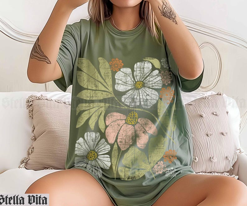 May include: A green t-shirt with a floral print featuring a variety of flowers in shades of pink, white, and yellow. The flowers are surrounded by green leaves and stems.