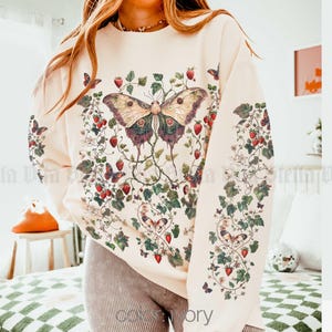 May include: A cream-colored sweatshirt with a floral print featuring butterflies and strawberries. The print is in shades of red, green, and brown.