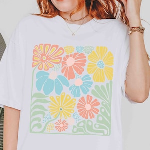 Peut inclure: T-shirt blanc avec un imprim&eacute; floral color&eacute;. Les fleurs sont dans des tons de rose, jaune, bleu et vert. L'impression est de forme carr&eacute;e et est centr&eacute;e sur le t-shirt.