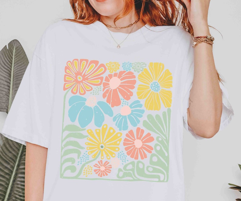 Peut inclure: T-shirt blanc avec un imprim&eacute; floral color&eacute;. Les fleurs sont dans des tons de rose, jaune, bleu et vert. L'impression est de forme carr&eacute;e et est centr&eacute;e sur le t-shirt.