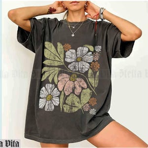 May include: A dark gray oversized t-shirt with a vintage floral print in shades of pink, white, green, and orange. The print features a large flower with a yellow center and smaller flowers and leaves.
