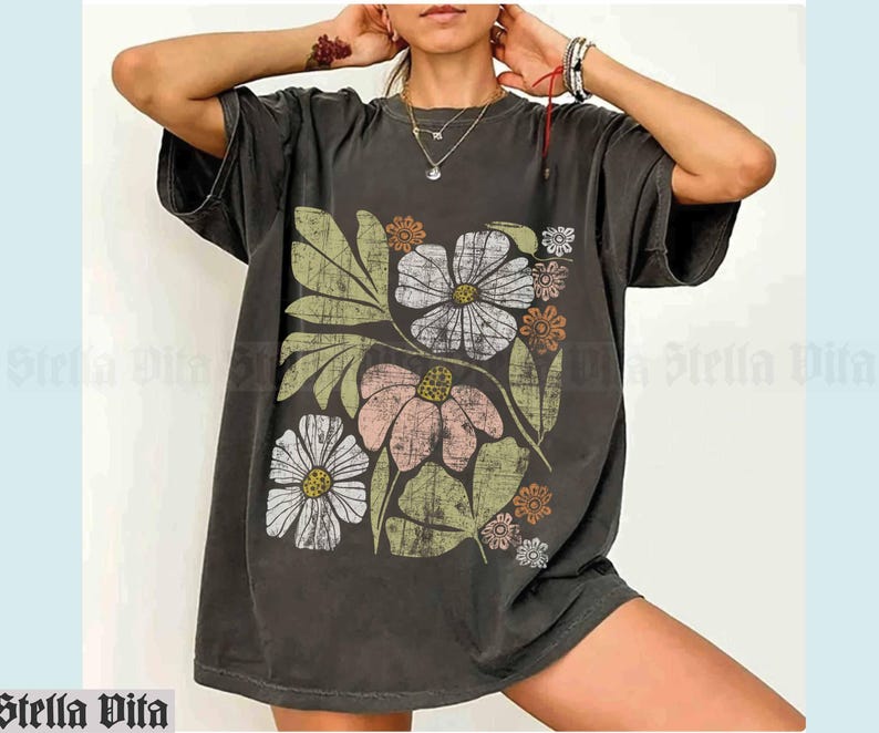 May include: A dark gray oversized t-shirt with a vintage floral print in shades of pink, white, green, and orange. The print features a large flower with a yellow center and smaller flowers and leaves.