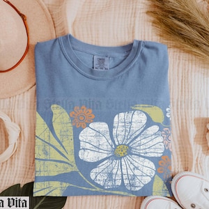 May include: A blue t-shirt with a vintage floral print in shades of white, yellow, and orange. The print features a large flower with a distressed look.