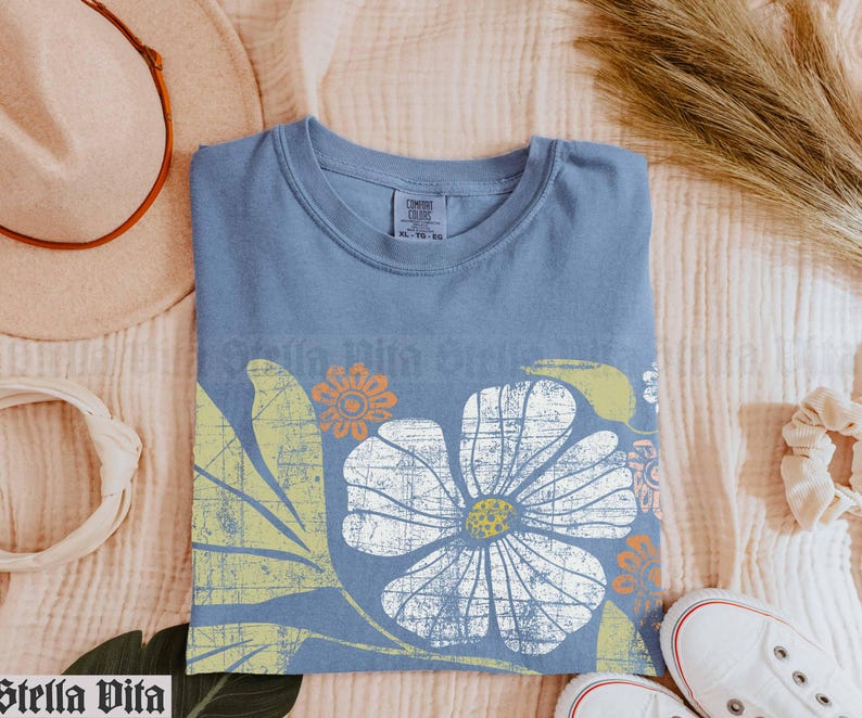 May include: A blue t-shirt with a vintage floral print in shades of white, yellow, and orange. The print features a large flower with a distressed look.