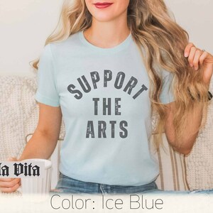 May include: A light blue t-shirt with the text "SUPPORT THE ARTS" in a distressed gray font.