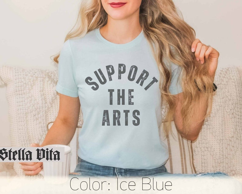 May include: A light blue t-shirt with the text "SUPPORT THE ARTS" in a distressed gray font.