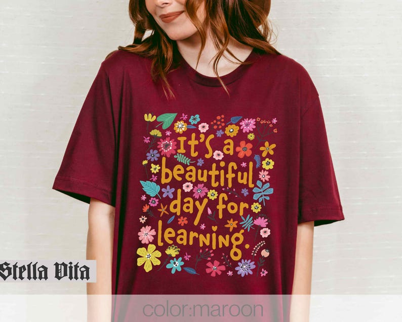 May include: A maroon t-shirt with a floral design and the text "It's a beautiful day for learning."