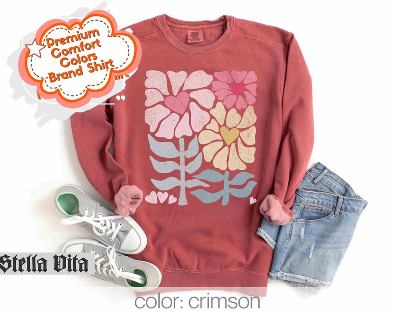 May include: Crimson red sweatshirt with a floral design featuring hearts and leaves. The design is in shades of pink, yellow, blue, and green.