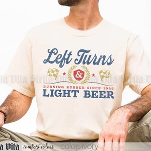 May include: Ivory-colored t-shirt with the text "Left Turns" in a vintage blue font. Below, it reads "Burning Rubber Since 1985 LIGHT BEER" in blue. The design includes racing flags and a laurel wreath.