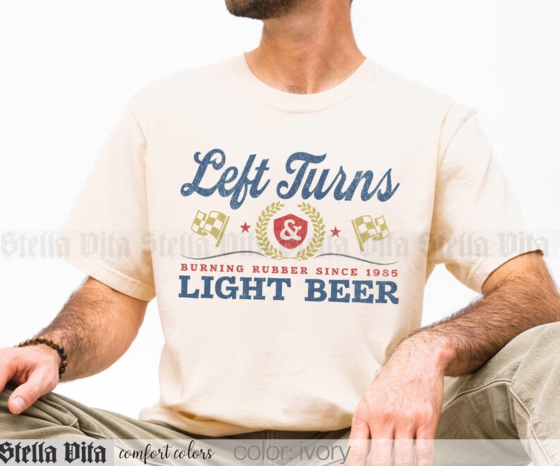 May include: Ivory-colored t-shirt with the text "Left Turns" in a vintage blue font. Below, it reads "Burning Rubber Since 1985 LIGHT BEER" in blue. The design includes racing flags and a laurel wreath.