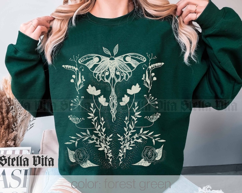 May include: Forest green sweatshirt with a white graphic of a moth and flowers. The text "color: forest green" is printed on the bottom of the sweatshirt.