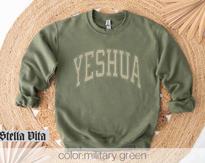 May include: A military green sweatshirt with the word "YESHUA" printed in a large, white, arched font.