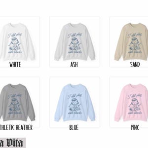 K&ouml;nnte beinhalten: Ein Set aus zehn Crewneck-Sweatshirts in verschiedenen Farben mit einem Motiv eines M&auml;dchens, das mit Bl&ouml;cken spielt, und dem Text "I still play with blocks". Die Farben umfassen Wei&szlig;, Asche, Sand, Sport-Heather, Blau und Pink.