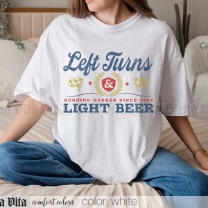 May include: White t-shirt with the text "Left Turns" in blue script above a graphic with flags and the words "Burning Rubber Since 1985 Light Beer". The shirt is a comfort color.