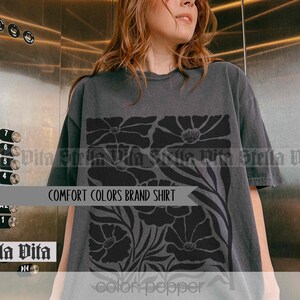 Puede incluir: Una camiseta gris oscuro con un dise&ntilde;o floral negro. El dise&ntilde;o presenta flores grandes y estilizadas con un patr&oacute;n repetitivo. El texto "COMFORT COLORS BRAND SHIRT" est&aacute; impreso en la camiseta.