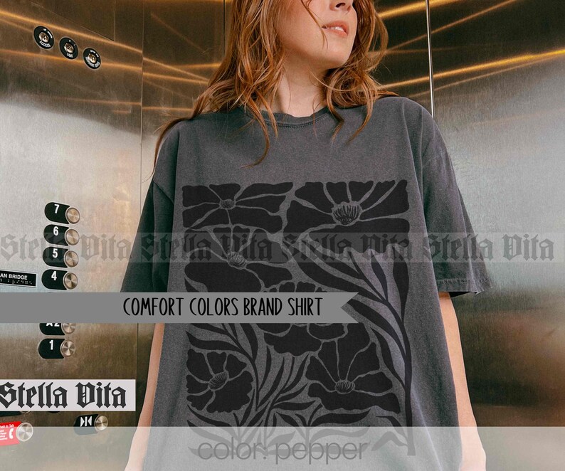 Puede incluir: Una camiseta gris oscuro con un dise&ntilde;o floral negro. El dise&ntilde;o presenta flores grandes y estilizadas con un patr&oacute;n repetitivo. El texto "COMFORT COLORS BRAND SHIRT" est&aacute; impreso en la camiseta.