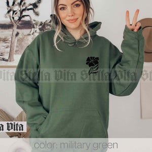 May include: A green hooded sweatshirt with a black floral design on the left chest. The text "color: military green" is at the bottom of the image.