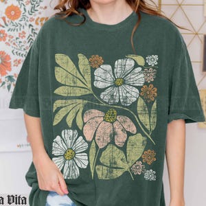 May include: A green t-shirt with a floral print featuring white, pink, and yellow flowers with green leaves. The flowers have a vintage, distressed look.