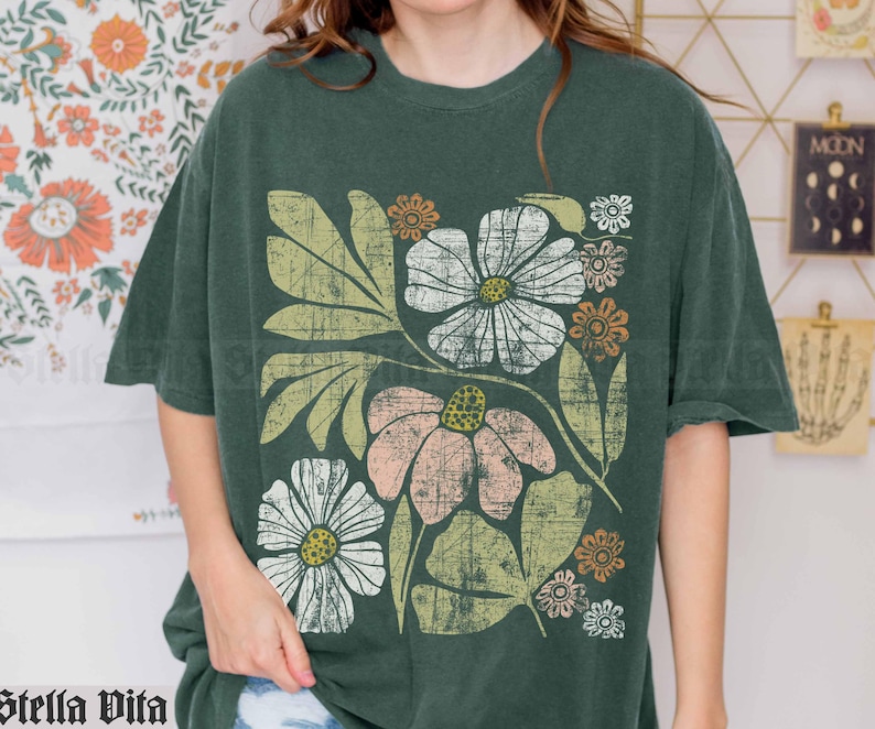 May include: A green t-shirt with a floral print featuring white, pink, and yellow flowers with green leaves. The flowers have a vintage, distressed look.