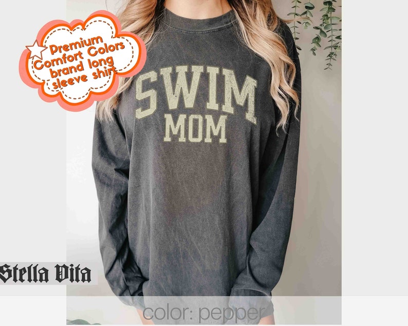 Puede incluir: Una camiseta negra de manga larga con el texto "SWIM MOM" en letras doradas. La camiseta est&aacute; hecha de una tela suave y c&oacute;moda.